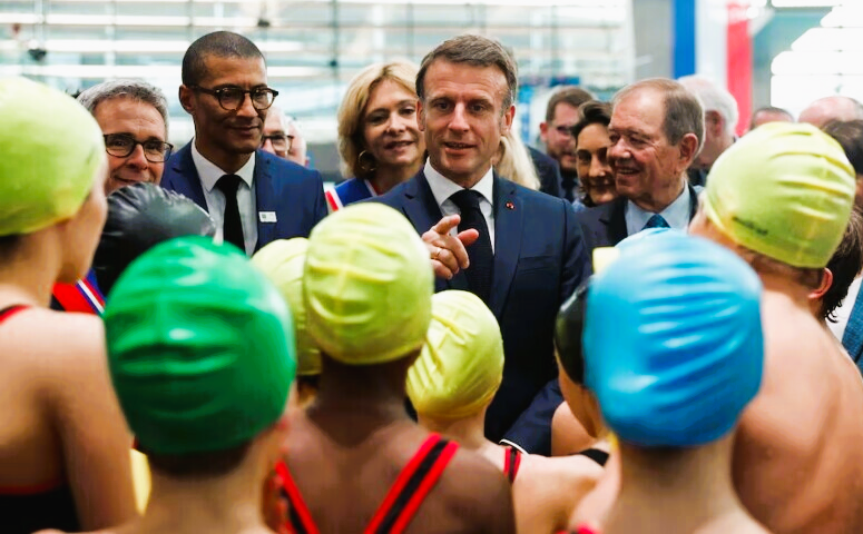 French President Emmanuel Macron talks to children after their swimming performance during the inauguration of the Olympic Aquatics Centre